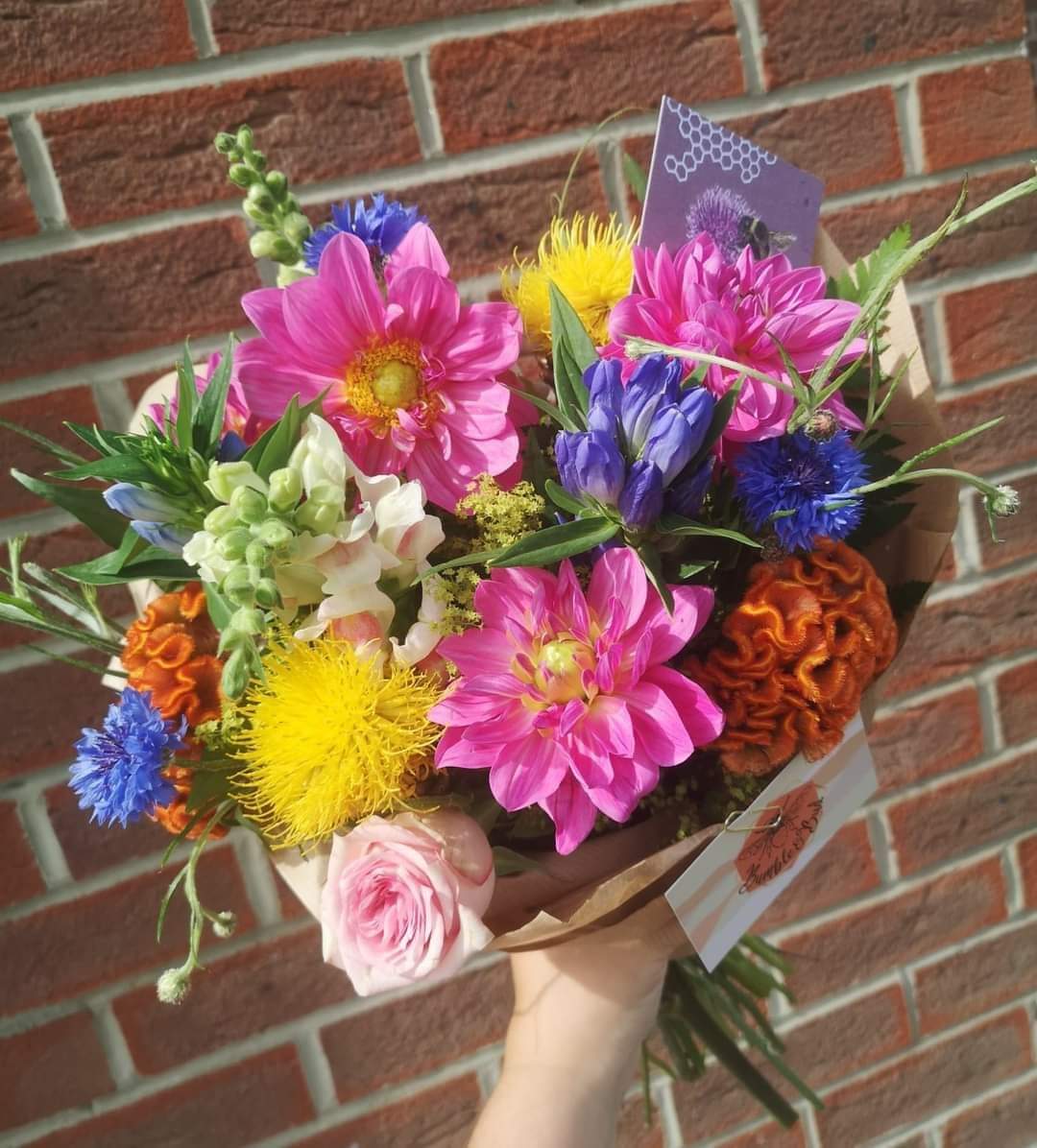 a bright bunch of flowers with a fresh mix of cerise dahlia stocks delphinium no foliage orange roses gift wrapped