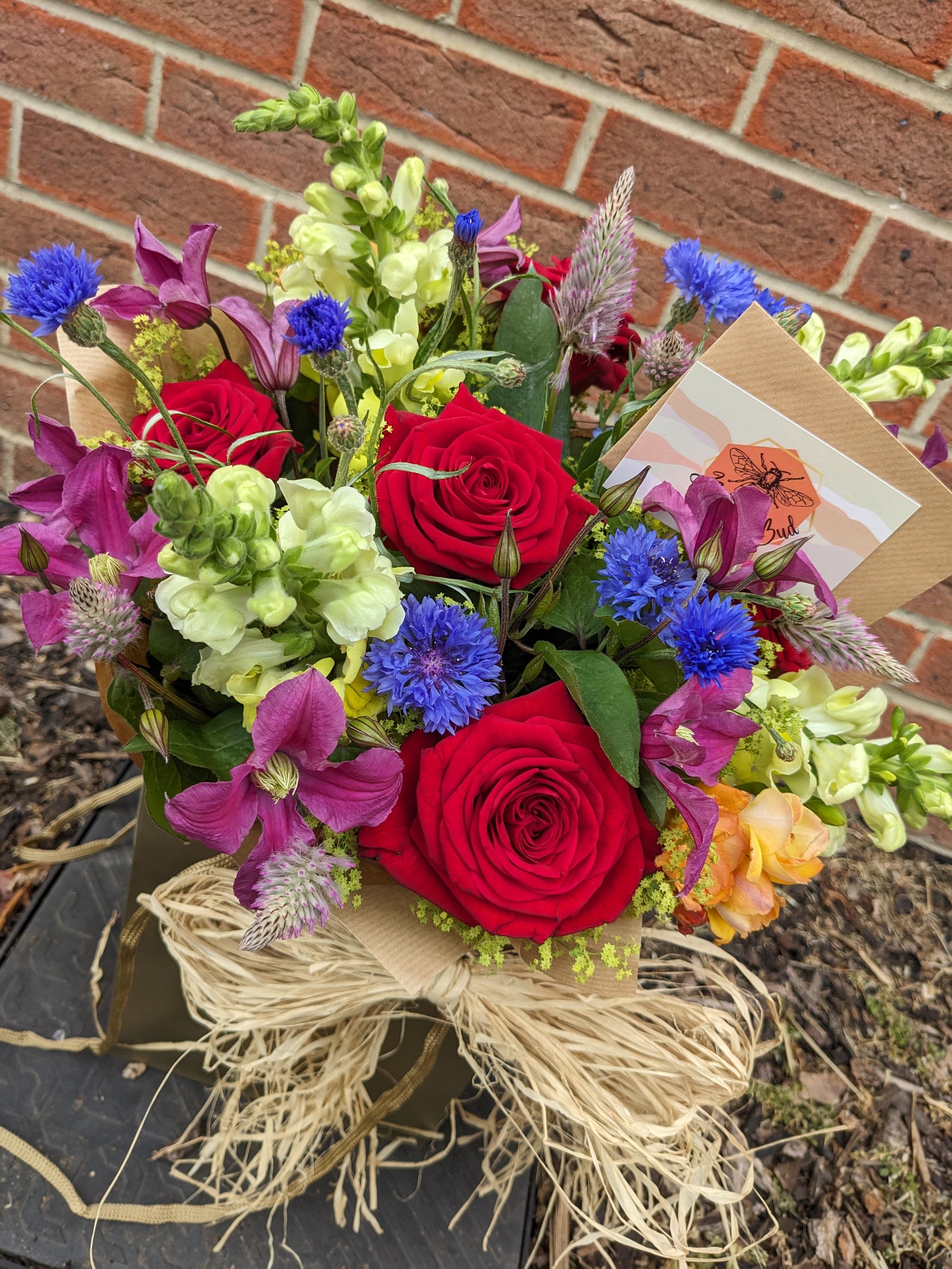 flower bouquet colourful red roses blue cornflower purple clematis yellow stocks gift wrapped in brown natural paper