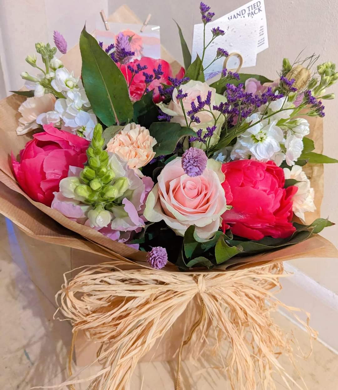 Flower bouquet- raffia bow fresh mix of seasonal flowers coral  peony, lilac rose , purple stocks, mixed green foliage .